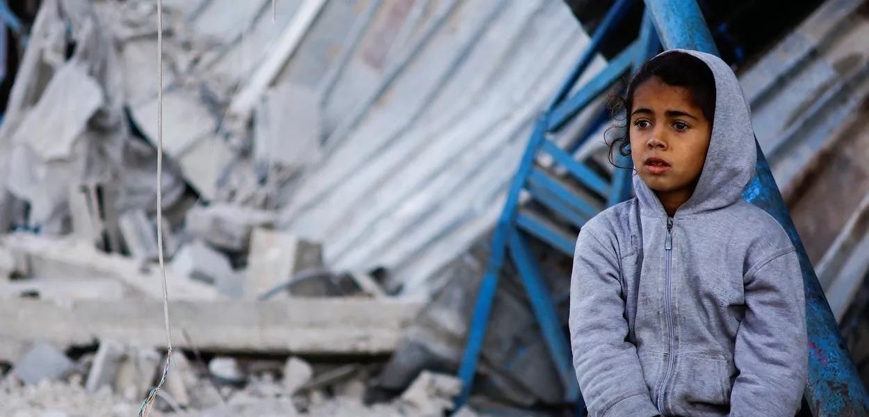 Criança palestina sentada no local de um ataque israelense a uma casa em Rafah, no sul da Faixa de Gaza (Foto: Reuters/Ibraheem Abu Mustafa)